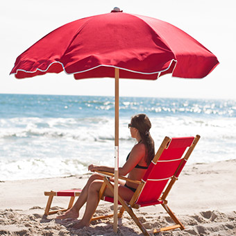Woman sitting at the ocean's edge under a red Frankford beach umbrella during the daytime