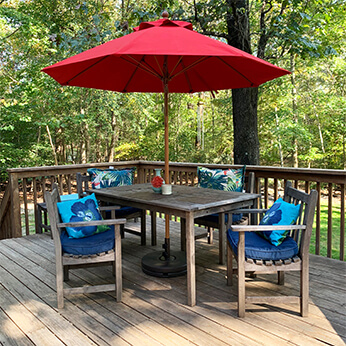 Red Frankford Monterey Umbrella shades a wooden table and chairs on a back deck in New Jersey