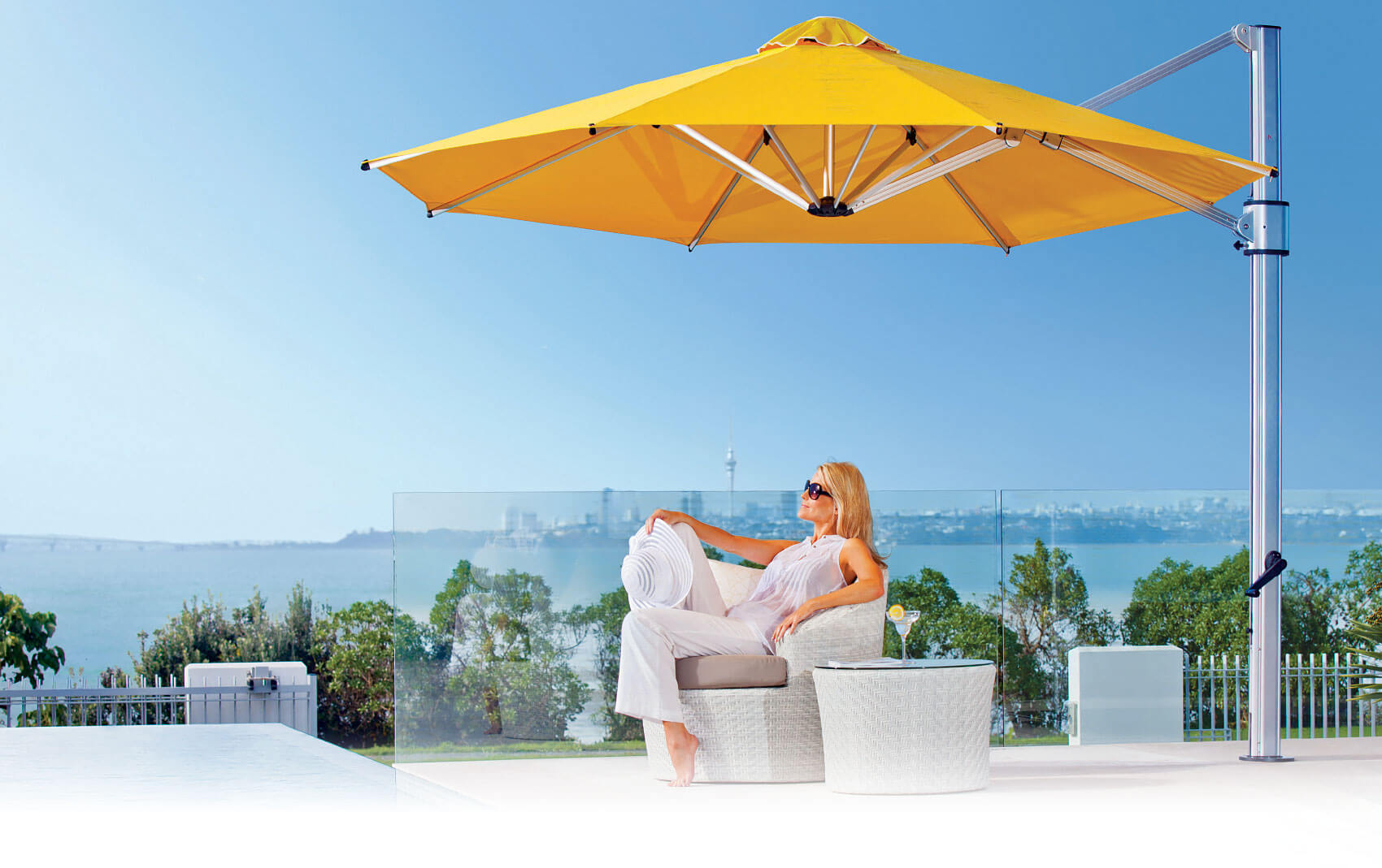 Woman relaxing under the shade of a yellow Frankford Cantilever umbrella in front of a city skyline