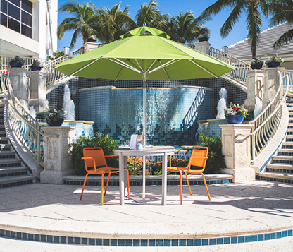 A green Frankford Greenwich Market Umbrella shades a table and chairs by a fountain at a resort in Naples
